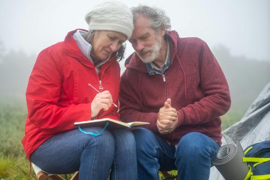 a man and woman sit in nature writing in a notebook