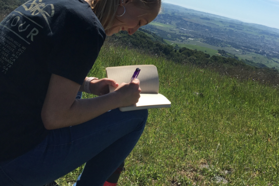 Student sitting in grassy field writing in notebook