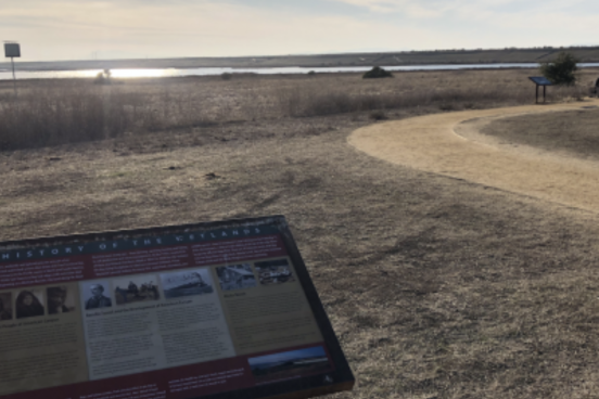a sign in front of a trail by a marsh