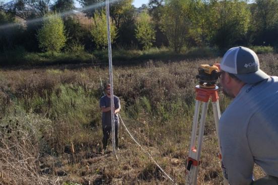 two students survey channel with transit and pole