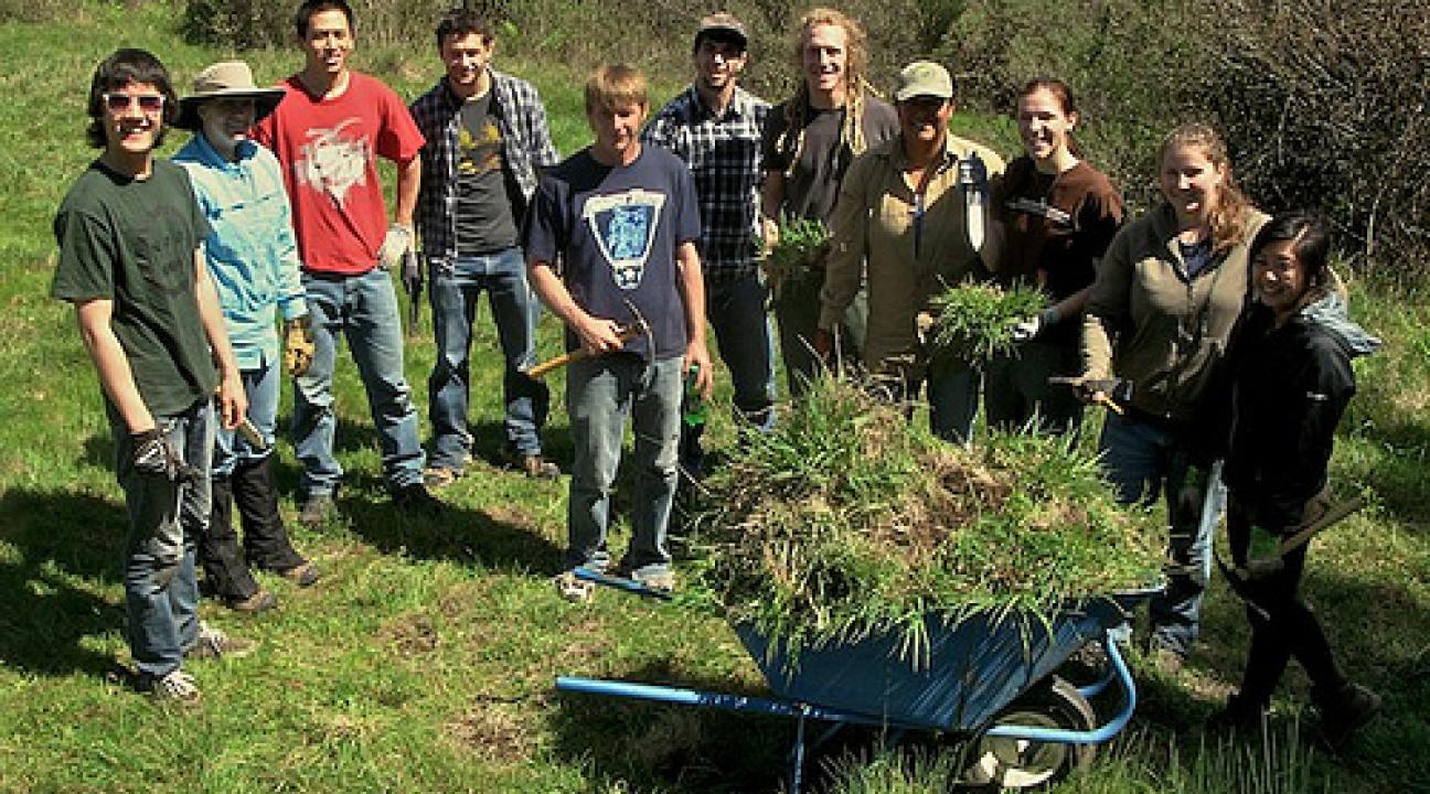 Students and wheelbarrow filled with removed weeds