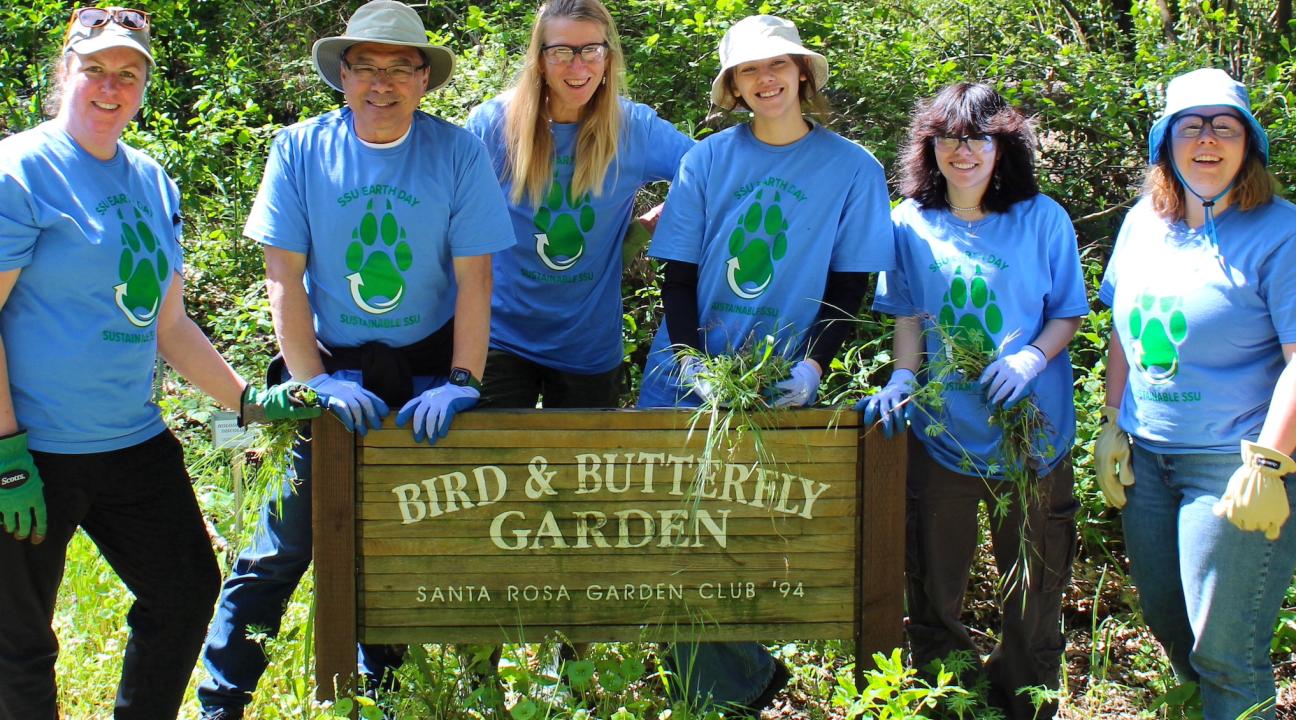 volunteers stand behind a sign for the butterfly garden