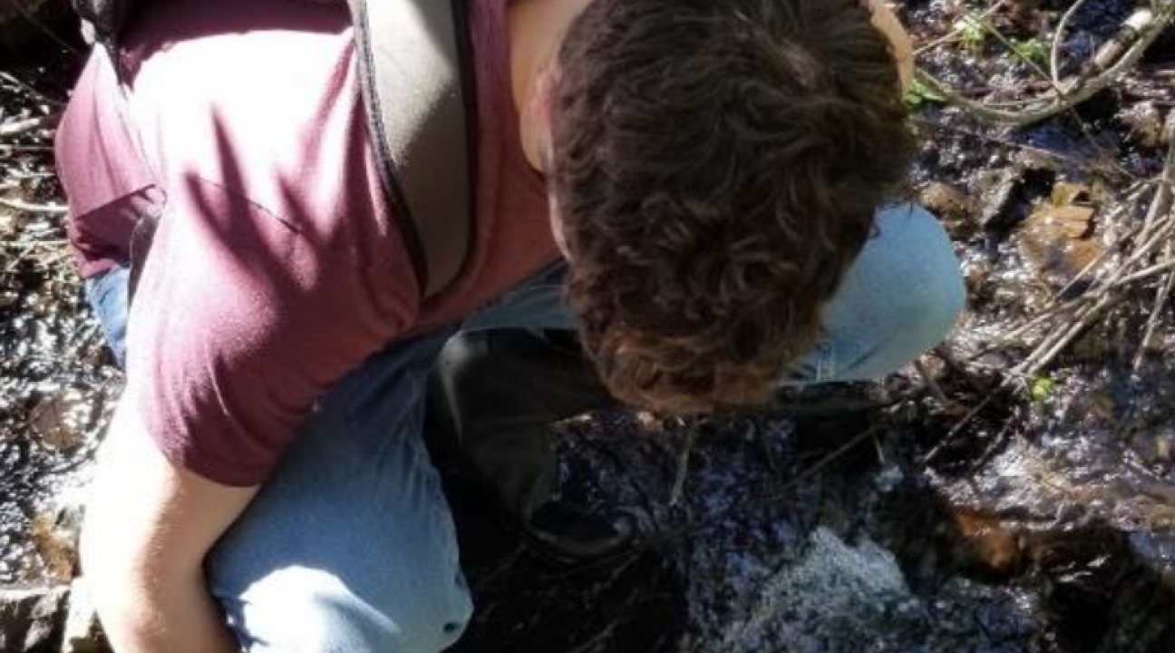 Student collecting water sample from stream