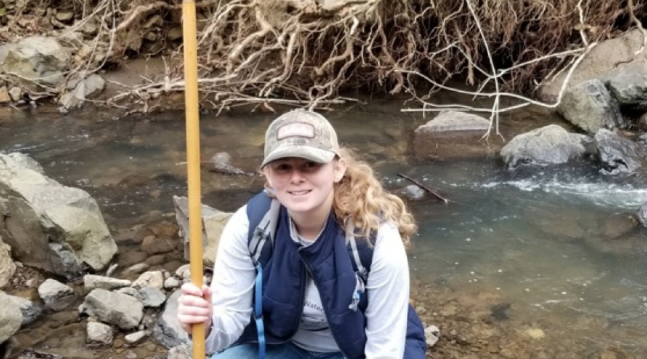 Student holding a d-net and kneeling in a creek