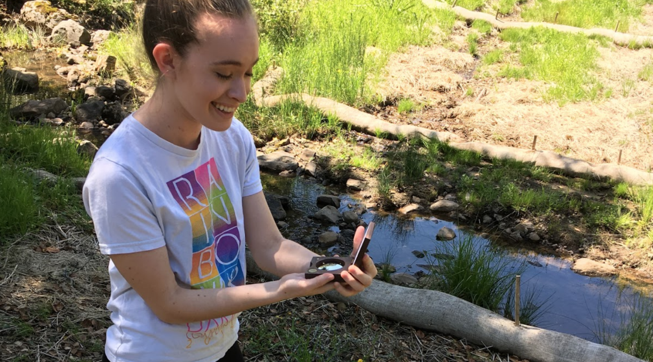 student holding a convex densiometer on a nature trail