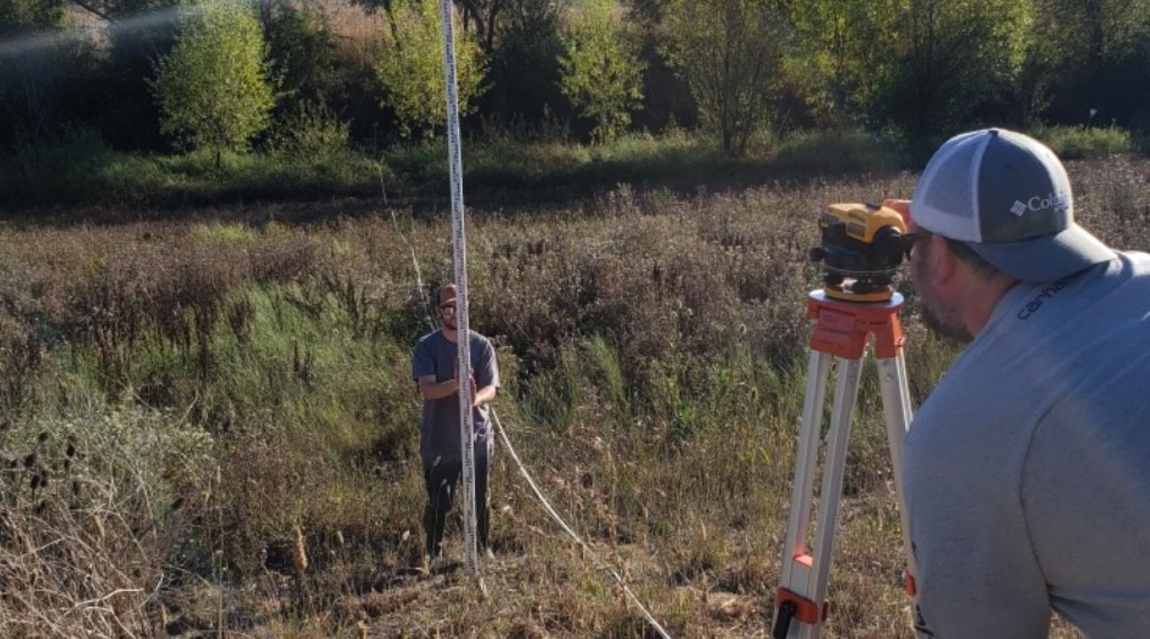 two students survey channel with transit and pole