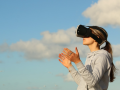 a woman wears VR goggles standing in front of sky and clouds