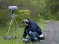Man crouches by sound recording equipment in grass