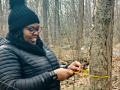 woman in winter clothes measuring a tree