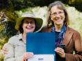 two nature educators stand outside holding an award