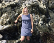 a woman with blonde hair stands in front of a rock with kelp