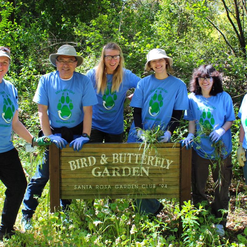 volunteers stand behind a sign for the butterfly garden