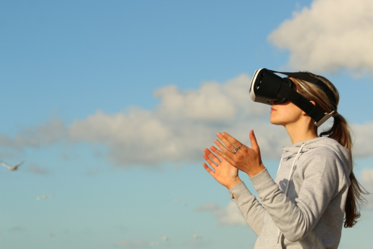 a woman wears VR goggles standing in front of sky and clouds