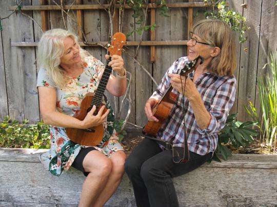 two women play ukuleles outside