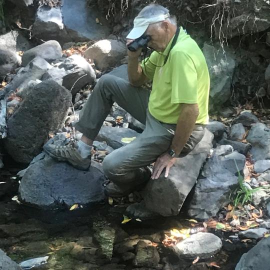 A man sits on a rock and looks through binoculars