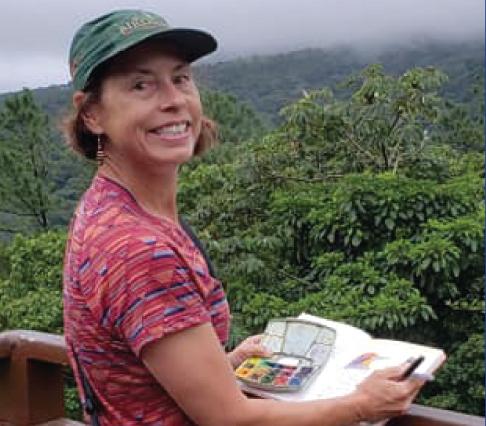 a woman holds a notebook and colored pens in front of a valley