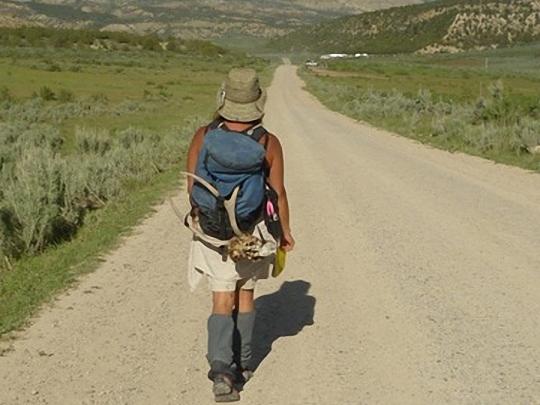 Woman walking on dirt road into mountains