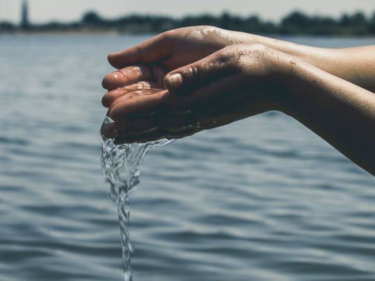 hands hold water as it pours out into river
