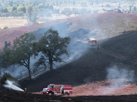 firetruck and helicopter on a smokiy burned hillside with firefighter hosing it down