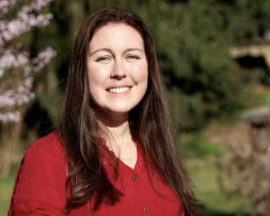 woman with long brown hair smiles at camera outside