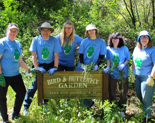 volunteers stand behind a sign for the butterfly garden