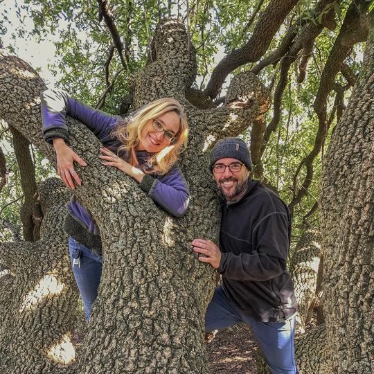 Leader TreeGirl and a colleague smile at the camera while embracing a tree