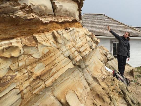 a woman stands and points at a sandstone cliff