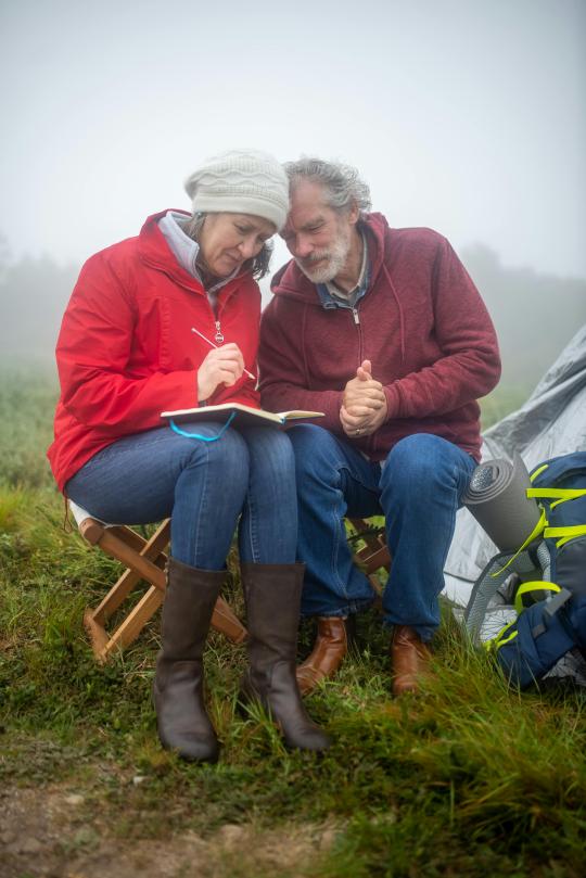 a man and woman sit in nature writing in a notebook