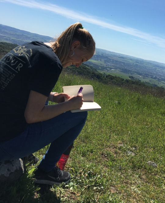 Student sitting in grassy field writing in notebook