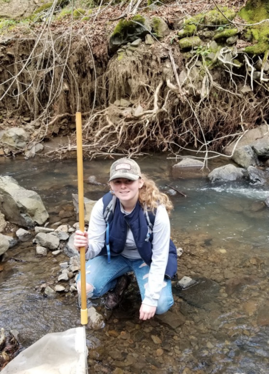 Student holding a d-net and kneeling in a creek