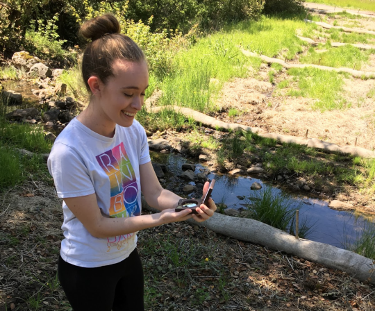 student holding a convex densiometer on a nature trail