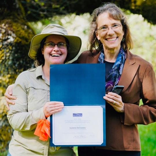 two nature educators stand outside holding an award