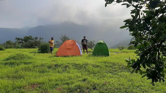 two people and tents on grass in front of a mountain