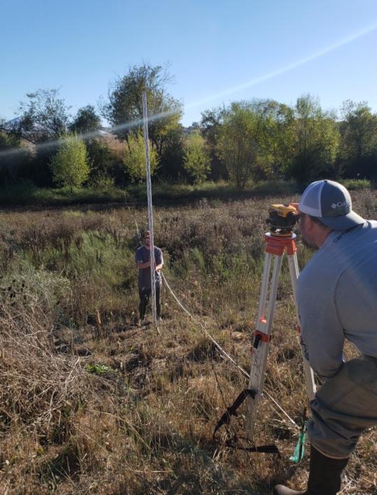 two students survey channel with transit and pole