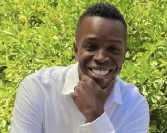 a man with dark skin and hair smiles at the camera